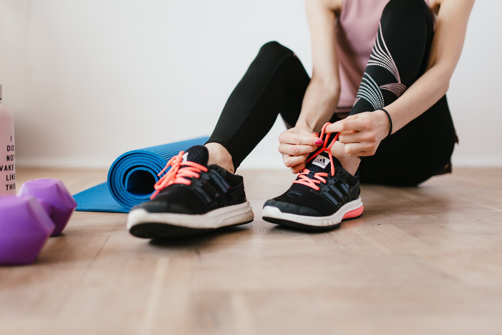 Anonymous slender female athlete tying shoelaces near sport accessories